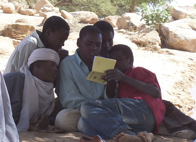 School boys read one of the first booklets written in the Omega language: a pocket calendar with proverbs